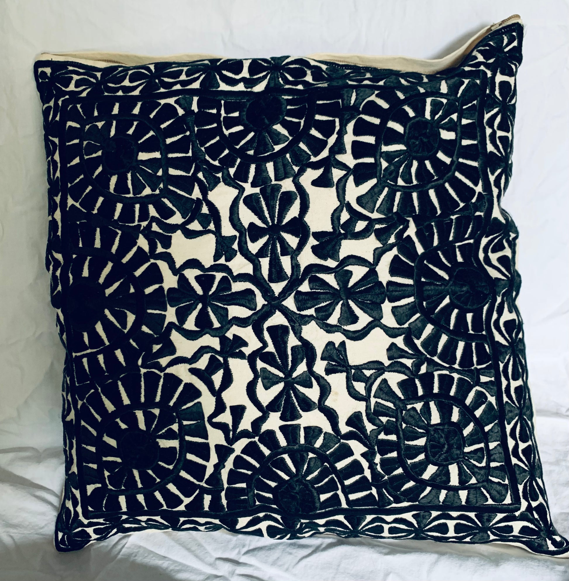 A square decorative throw pillow with a black hand-embroidered floral and geometric pattern on a cream background,