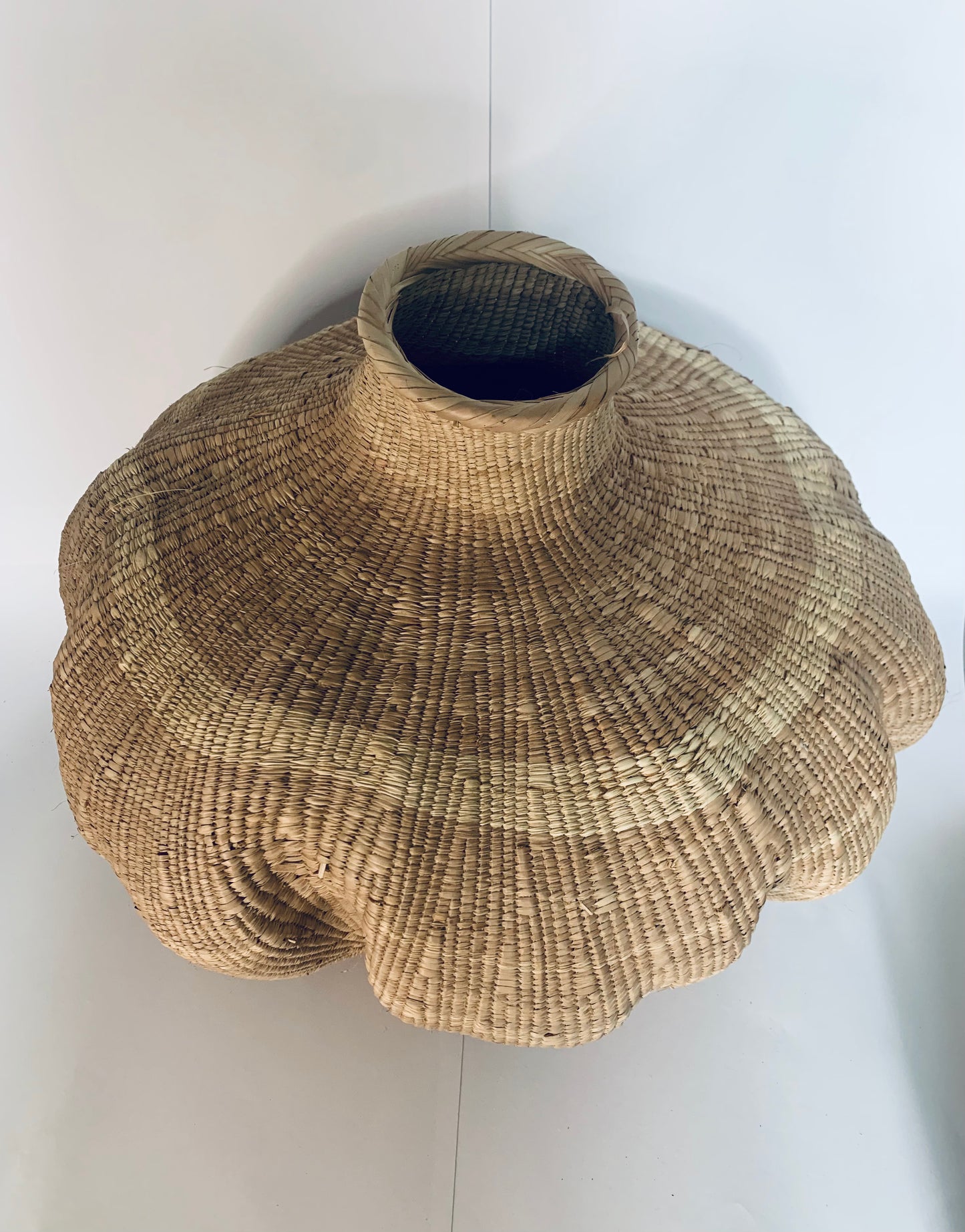 A hand-woven natural fiber basket with a wide, flared scalloped rim and a narrow neck opening, shown against a plain white background.
