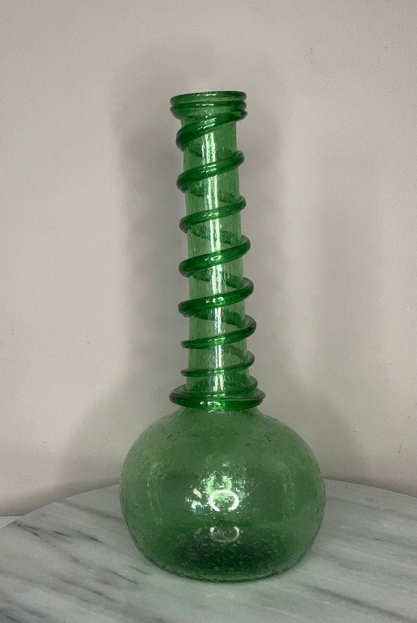 Hand-blown emerald green recycled glass bud vase with air bubbles throughout and a spiral decoration along the neck, finished with a pontil mark.