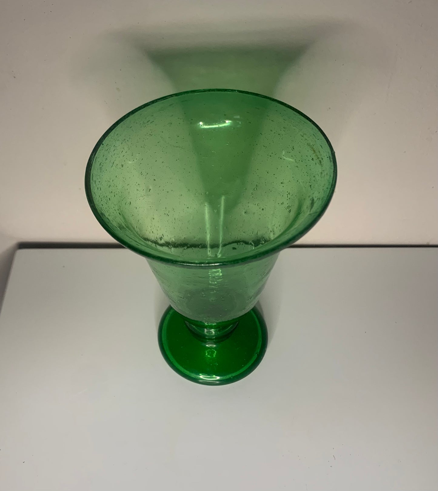 A green glass pedestal glass with a flared rim and a round base.