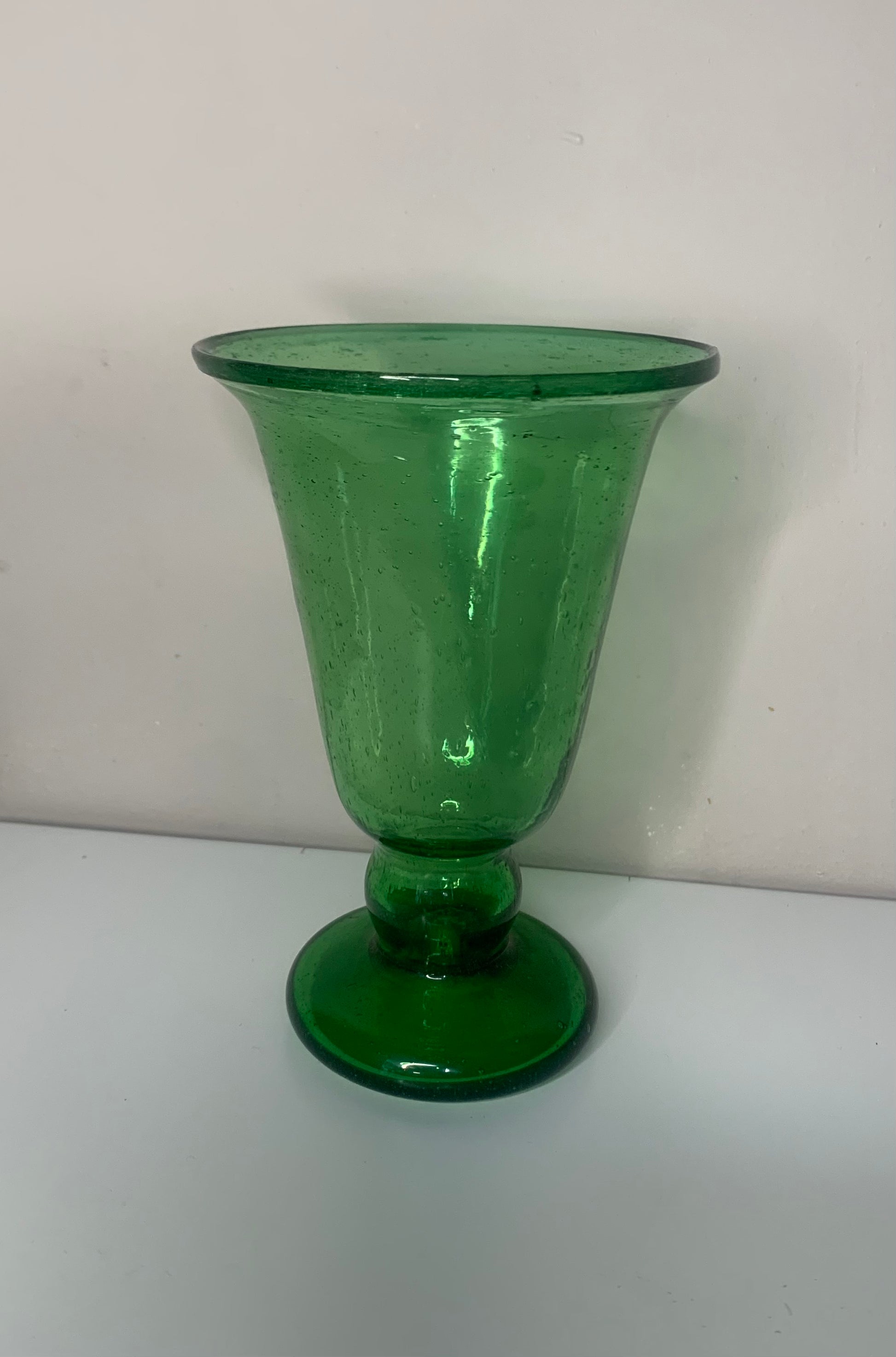 A green glass pedestal glass with a flared rim and a round base.