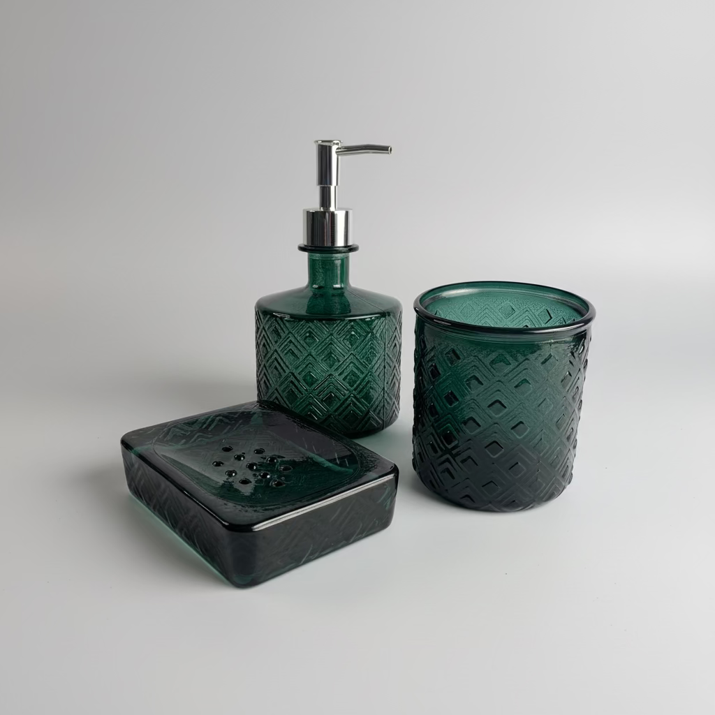 A three-piece green glass bathroom set featuring a soap dispenser with a silver pump, a matching toothbrush holder, and a rectangular soap dish with a lid, all with an embossed diamond pattern on a white draped fabric background.