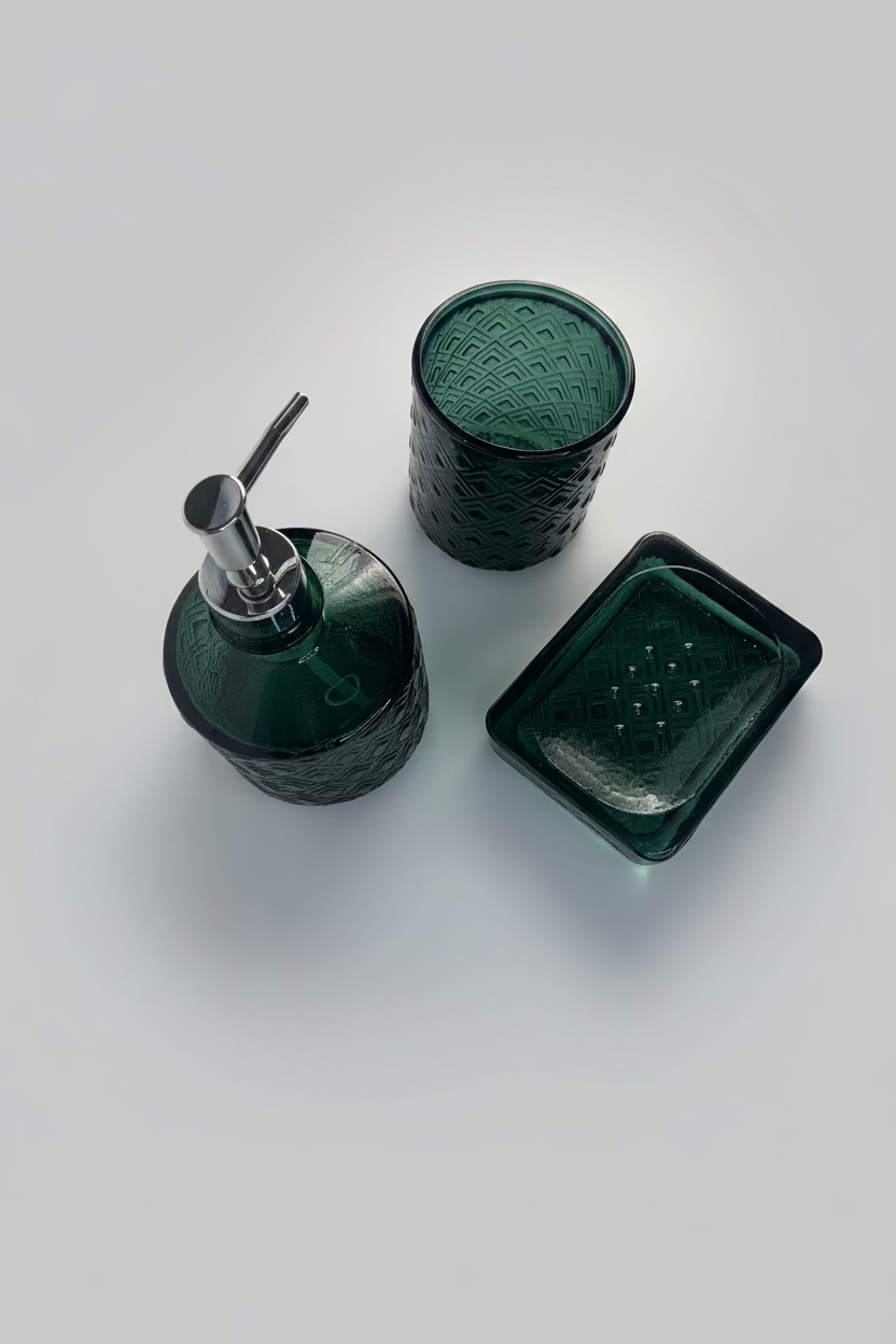 Three-piece dark green glass bathroom set including a soap dispenser with a silver pump, a textured glass cup, and a rectangular glass tray, arranged on a white fabric background.